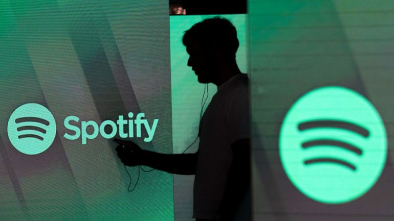 A man checks his smartphone whilst standing amongst illuminated screens bearing the Spotify Technology