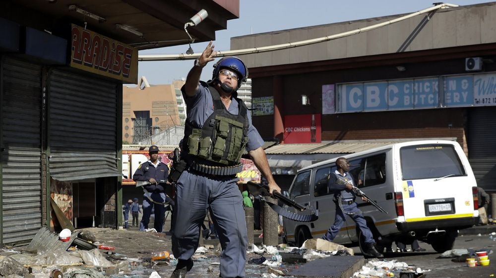 A riot police officer throws a tear gas canister as looters make off with goods from a store in east Johannesburg