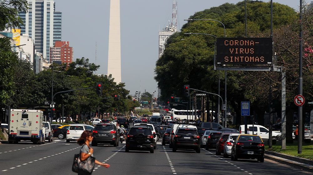 A woman walking in front of an electronic board displaying a message that reads ‘coronavirus symptoms’ in Buenos Aires, Argentina