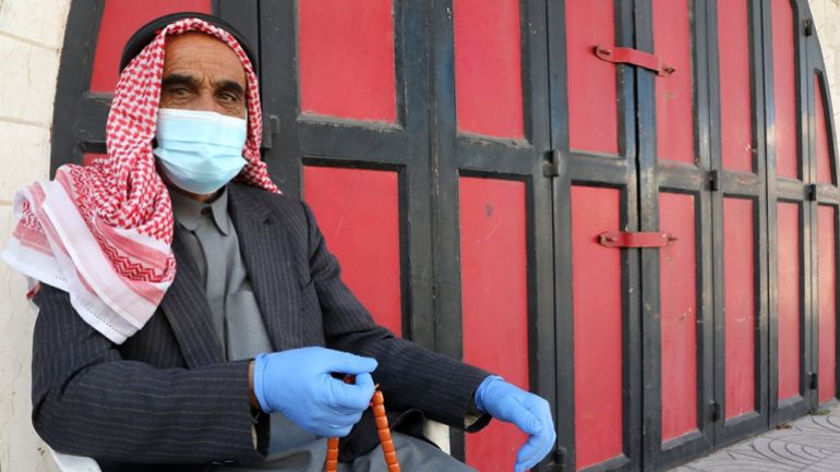 An elderly Palestinian sits with mask and latex gloves outside a closed shop in Hebron in the occupied West Bank on July 2, 2020