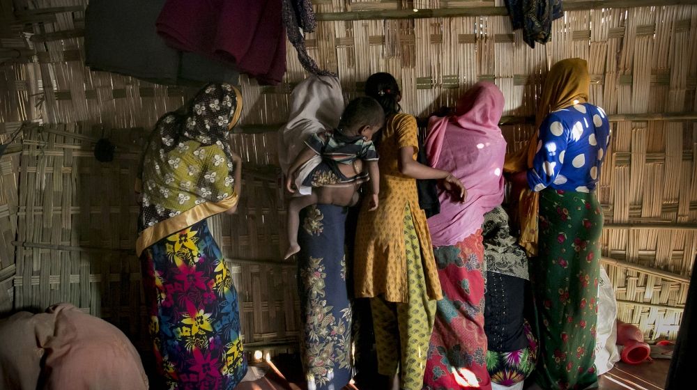 Women peer through the wall separating men from women during the wedding of Farmina Begum, 16, to 18-year-old Hashimullah, in a refugee camp in Cox’s Bazar, Bangladesh. An IOM investigation recently uncovered accounts of Rohingya girls as young as 11 getting married and families forcing girls to marry early to reduce the number of mouths to feed