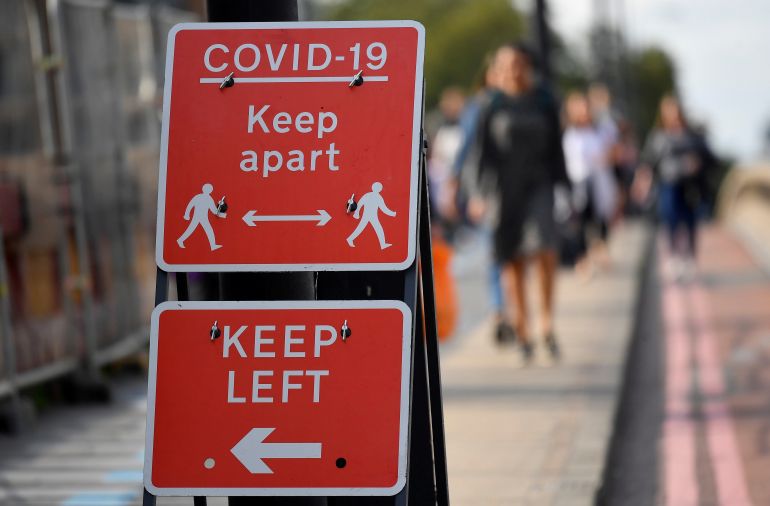 Pedestrians walk near public health signs in London, Britain