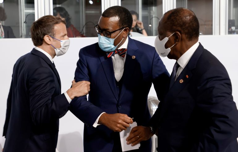 French President Emmanuel Macron grabs the president of the African Development Bank Akinwumi Adesina next to Ivory Coast President Alassane Ouattara, right, before the opening session of Tuesday’s summit