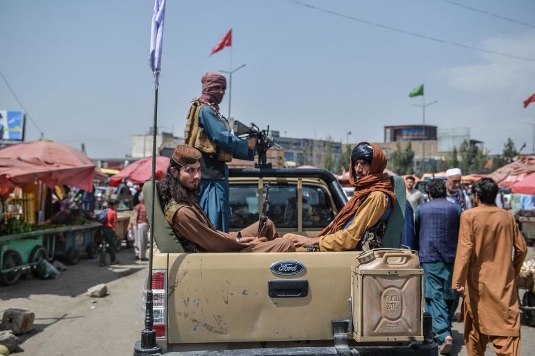 Taliban fighters on a pick-up truck move around a market area, flocked with local Afghan people at the Kote Sangi area of Kabul on August 17, 2021