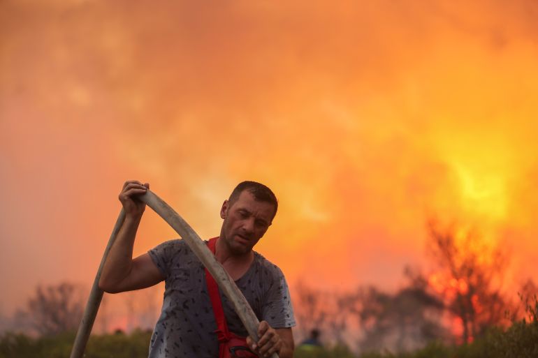 A volunteer firefighter holds a hose during a wildfire at Varympompi suburb north of Athens, Greece