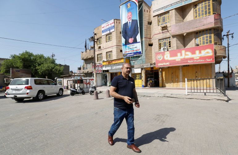 Moayad al-Azerjawi, an independent candidate in the parliamentary elections, walks near his poster in the Sadr City district of Baghdad on Tuesday