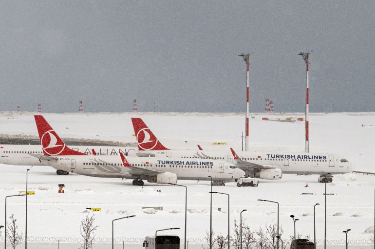 Aircrafts are parked on the tarmac of Istanbul airport, where flights are cancelled due to blizzard and heavy snowfall, in Istanbul, Turkey, on January 25, 2022. - Europe's busiest airport in Istanbul delayed its reopening and Greece declared a public holiday as the eastern Mediterranean neighbours began digging themselves out of a rare snowstorm that ground their capitals to a halt.