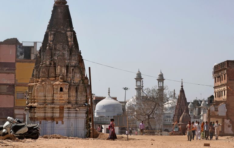 Gyanvapi Mosque, the white structure between Hindu temples, seen in the background as Hindu devotees walk at the site of a proposed grand promenade in Varanasi