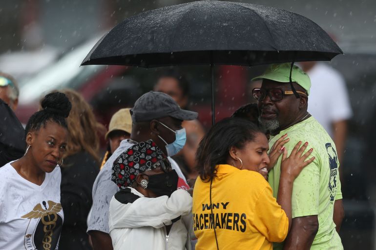 Bystanders gather under an umbrella as rain rolls in after a shooting at a supermarket on Saturday, May 14, in Buffalo, New York, US