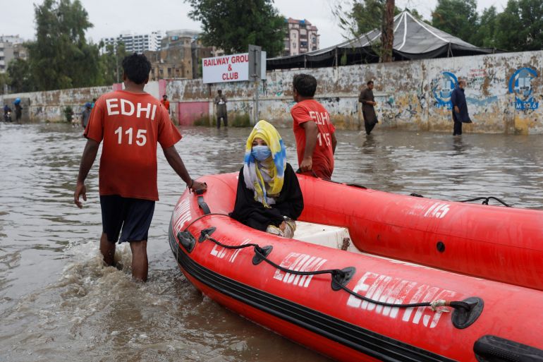 A woman sits in a rubber boat as volunteers pull through a flooded road during the monsoon season