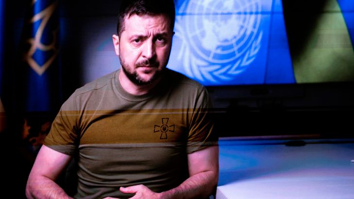 Volodomyr Zelenskyy in trade mark khaki green t-shirt with a Ukraine flag and UN logo behind him addresses the UN General Assembly in a video speech.