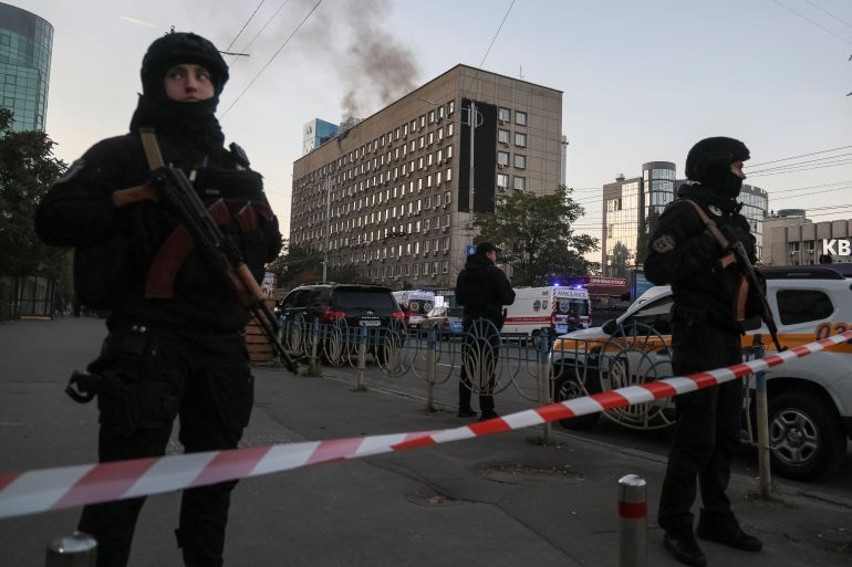 Soldiers stand behind police tape as smoke rises from a building behind them