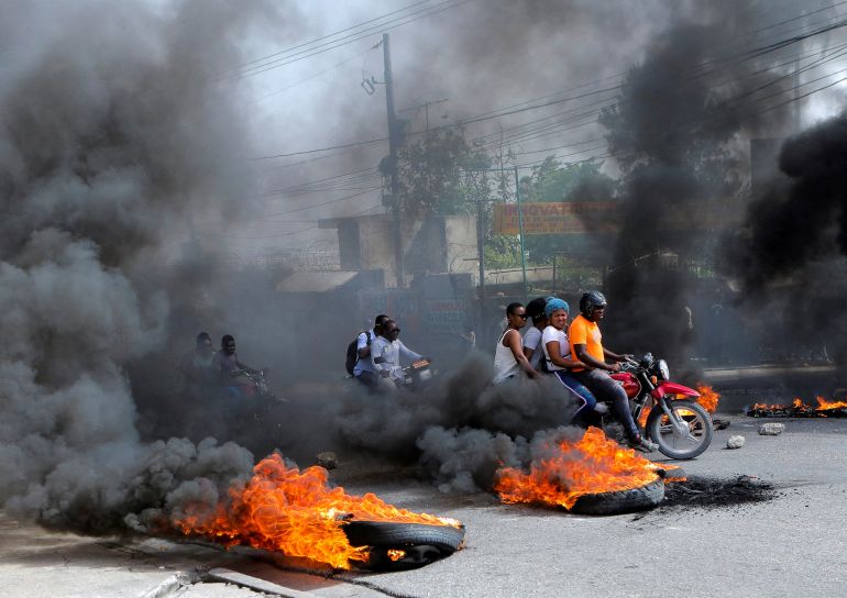 Motorcycle drivers pass through a burning roadblock as anger mounted over fuel shortages that have intensified as a result of gang violence, in Port-au-Prince, Haiti