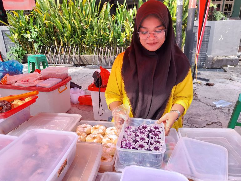 Naila holds a plastic container filled with fuchsia-coloured takjil. She is smiling.