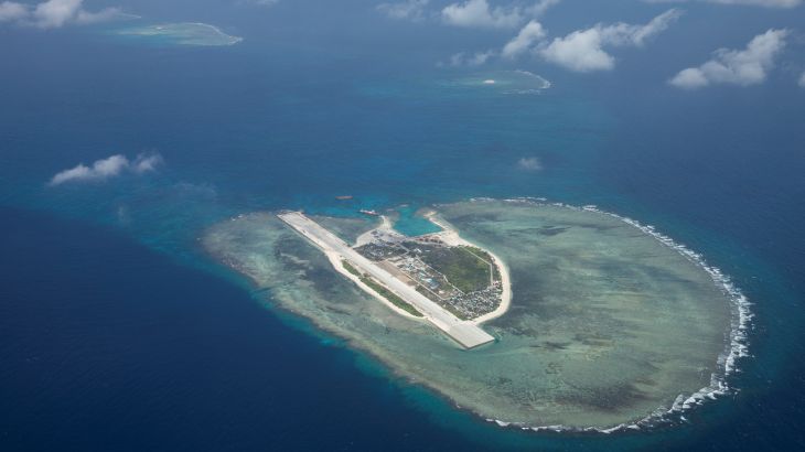 An island, seen from above, in the midst of a vast sea. A runway can be seen on the island.