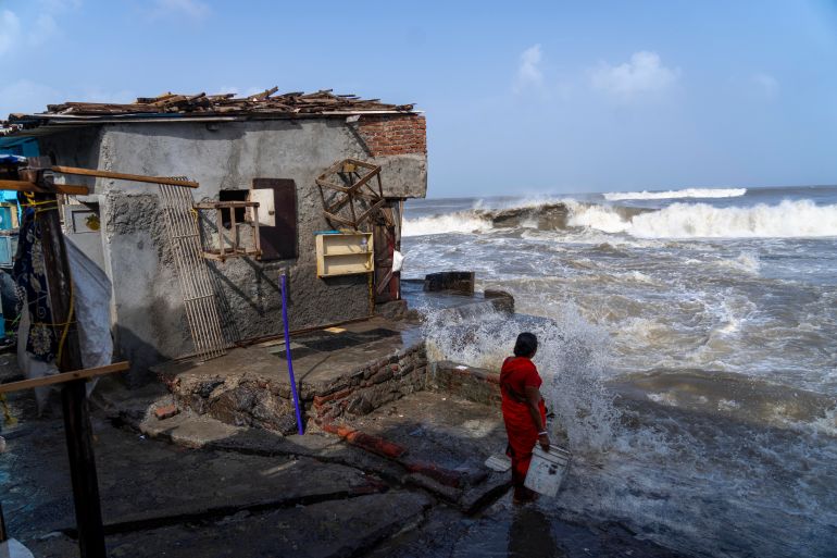 A woman stands next to her house as large waves hit Mumbai
