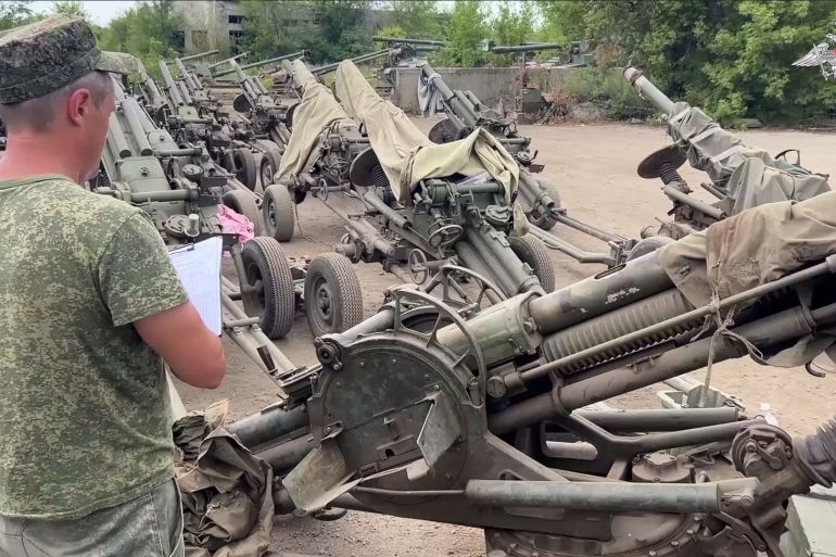 A military official checking howitzers transferred from the Wagner group. He has a clip board and is writing.