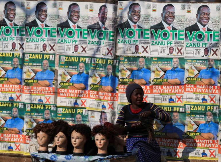 A wig salesperson sits beneath campaign ads in the capital Harare on August 25, as vote tabulation in the general elections continue