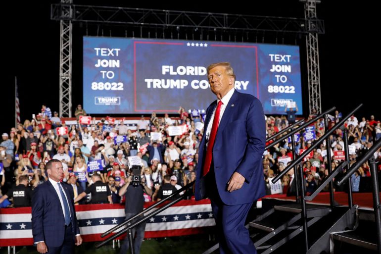 Trump, in a blue suit and red tie, walks down a metal staircase in front of a crowd of supporters, who cheer in front of a sign that reads: "Florida is Trump country"