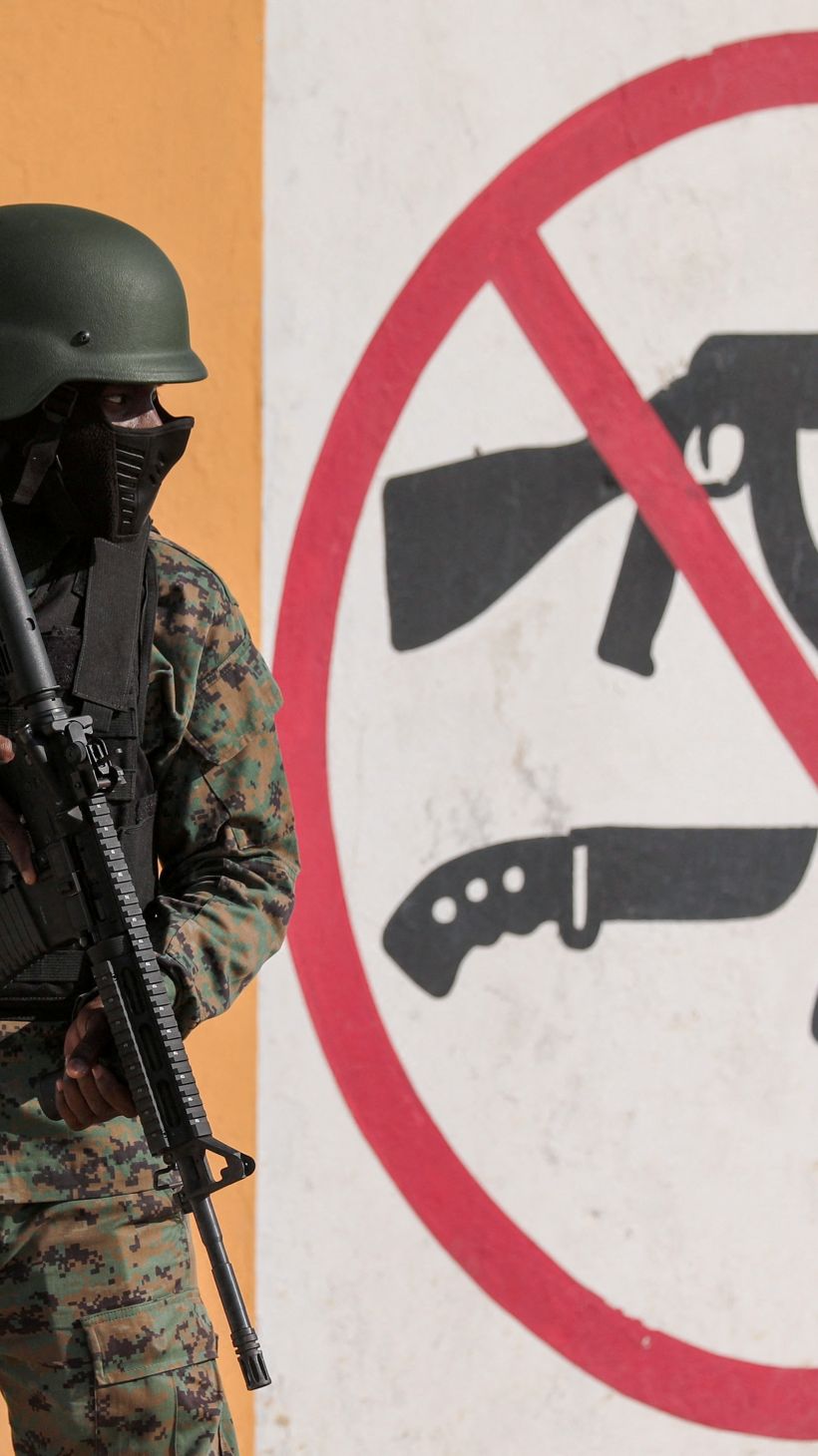 A soldier stands next to a mural prohibiting the use of firearms