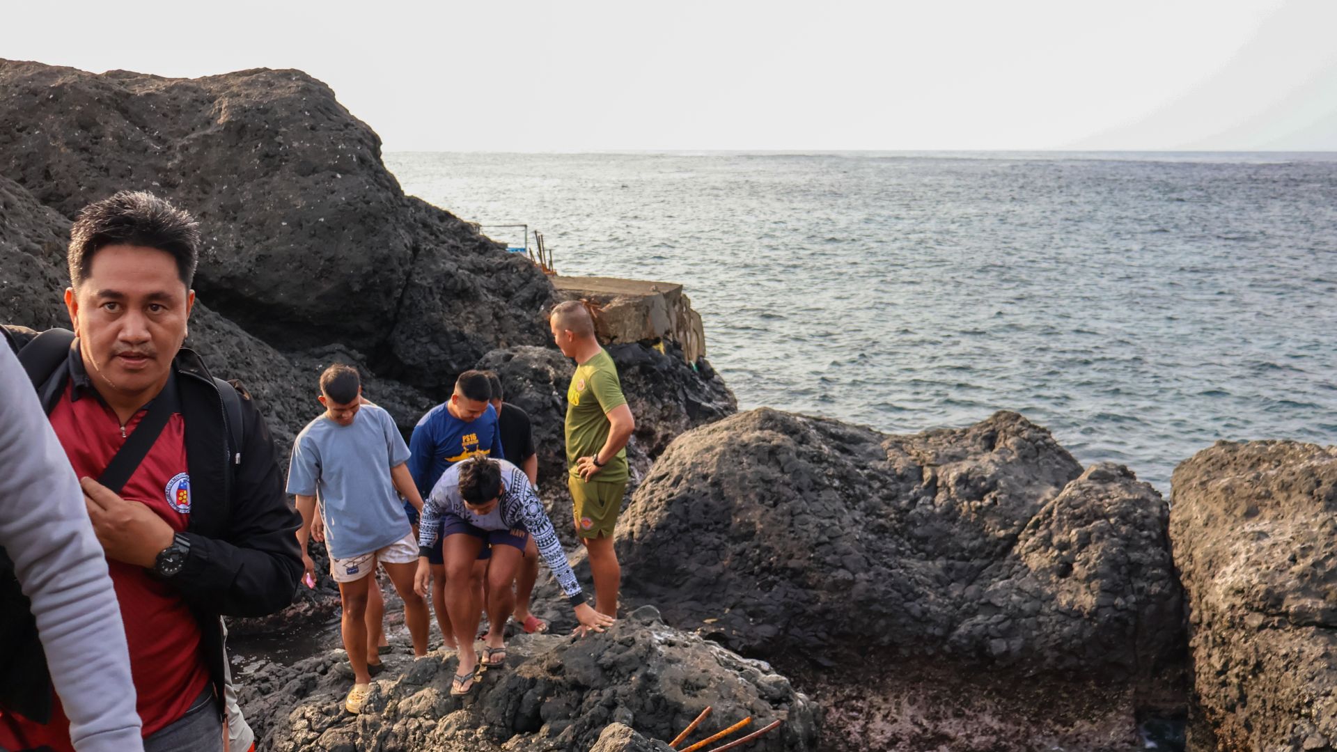 Soldiers and volunteer reservists clamber over jagged rocks to get ashore on Mavulis. The sea is behind them. The going looks rough.