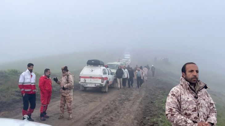 Rescue workers and their vehicles on a muddy mountain track. There is dense fog