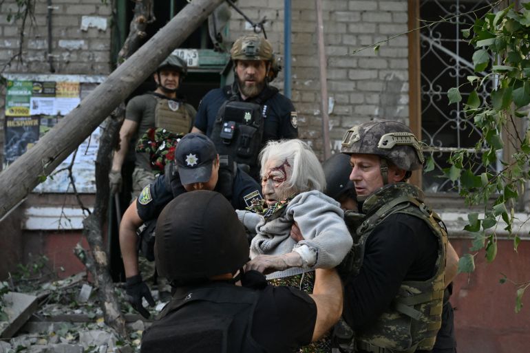 Rescuers helping an elderly woman after her apartment was hit by a Russian bomb. She has blood and dust on her face