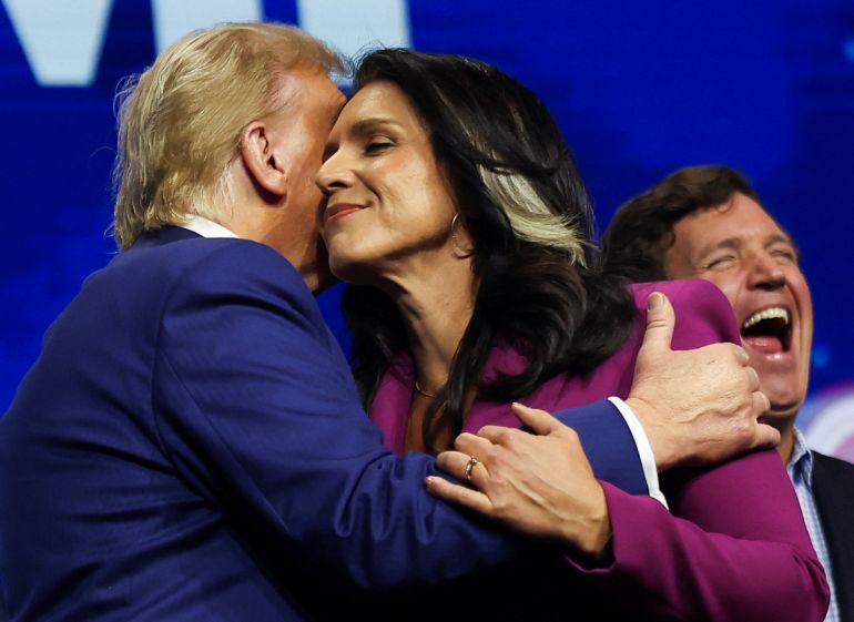 President-elect Donald Trump and former US Representative Tulsi Gabbard embrace, joined by Tucker Carlson, onstage at a campaign event sponsored by conservative group Turning Point USA