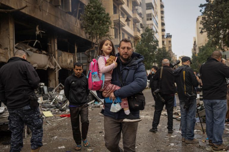 A man carries his daughter to her school as he walks past a damaged building in Beirut