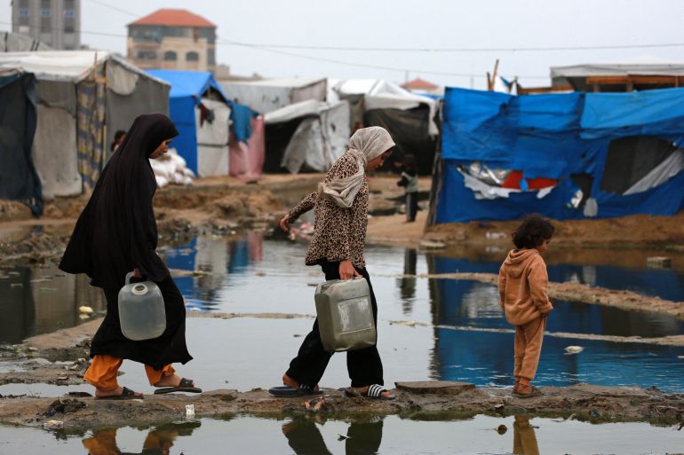 Displaced Palestinian women use a dry path to carry water