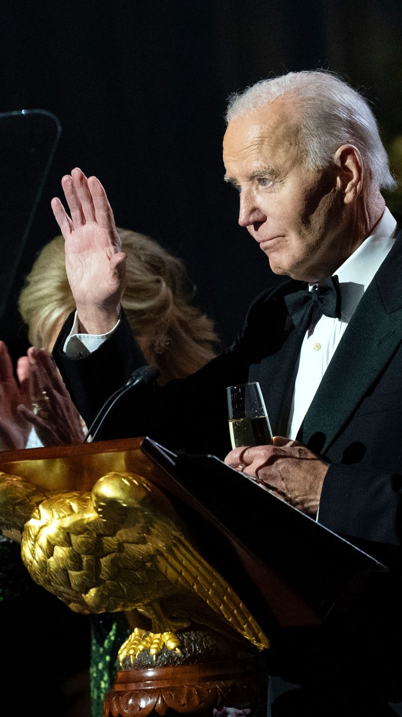 Joe Biden waves from behind a podium with a golden eagle at its base.