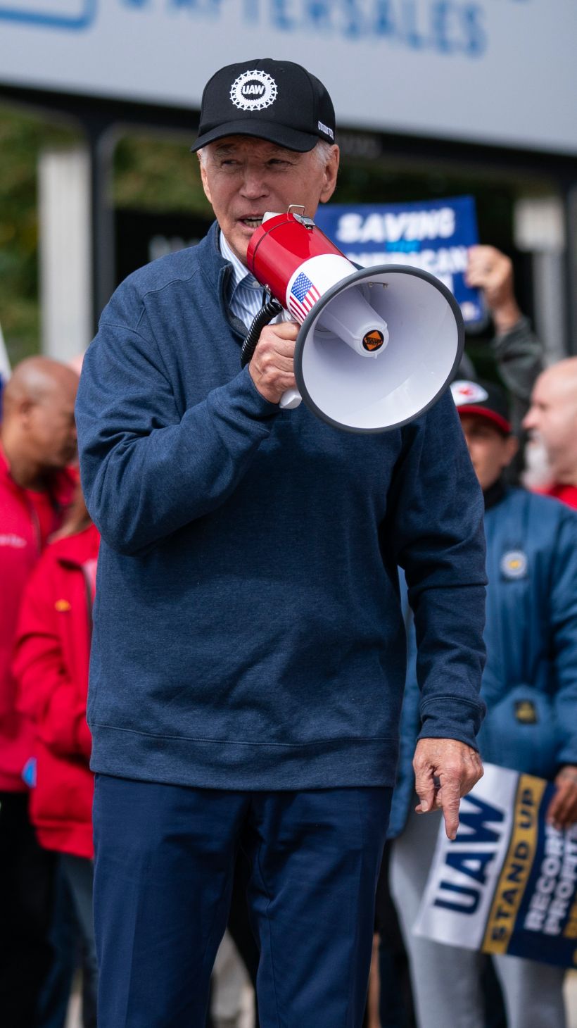 Joe Biden stands amid labour protesters, speaking into a microphone.