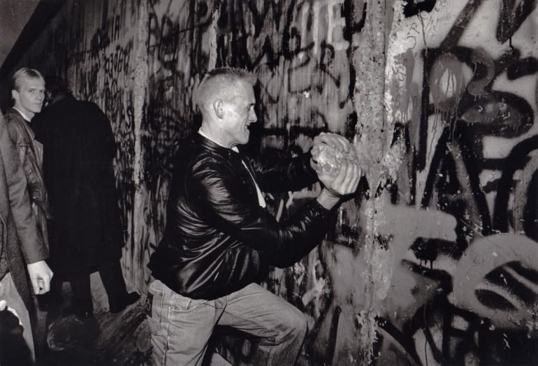 A young man takes a large piece of the Berlin Wall in his hands as he tries to hammer a hole in the wall with it, November or December 1989