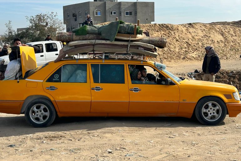 A yellow car with a mattress and other goods fastened on top
