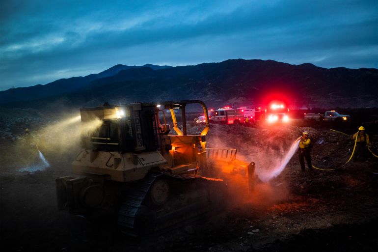 Forest Service firefighters receive help from a bulldozer to battle 26-32mph Santa Ana wind gusts while putting out the Duncan Fire that had burned 150 acres, at dusk on Wednesday, December 23, 2020 in Fontana, California