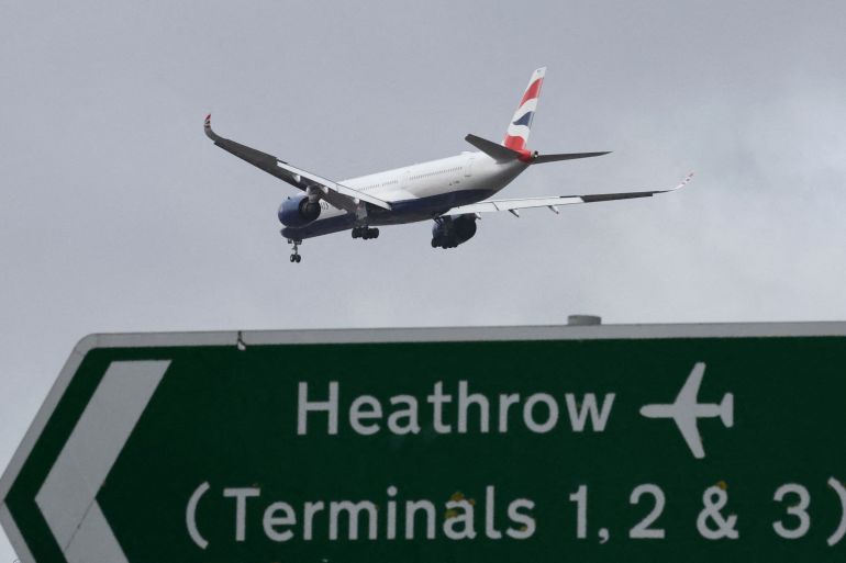 A British Airways passenger plane flies over a road direction sign as it makes its landing approach to Heathrow Airport in west London