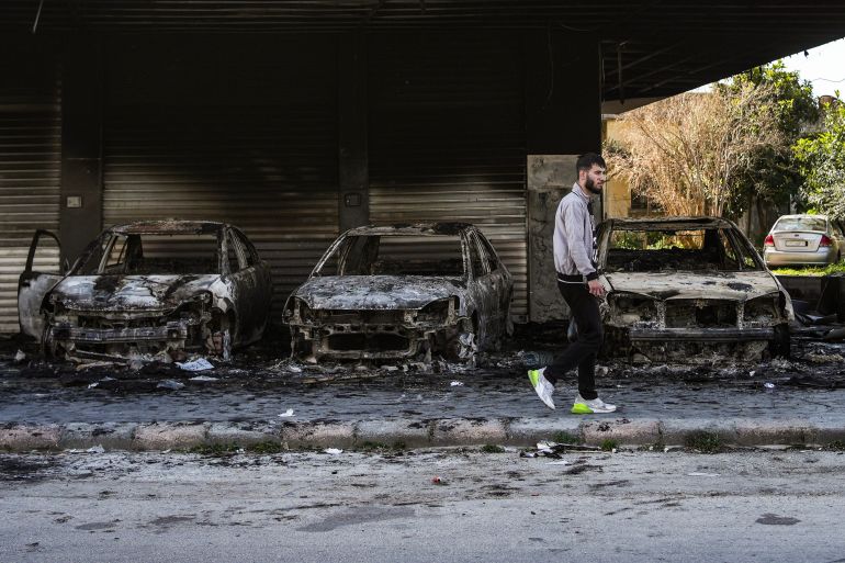 A man walks past burned-out cars in Jableh, 25km south of Latakia, following violence between Syrian security forces and armed fighters loyal to al-Assad on Syria’s coast, on March 20, 2025