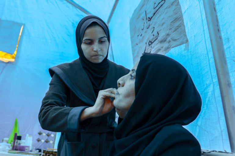 Amani, seated, says: ‘Looking after myself changes my mood,’ as Noor works on her face [Abdelhakim Abu Riash, Al Jazeera]