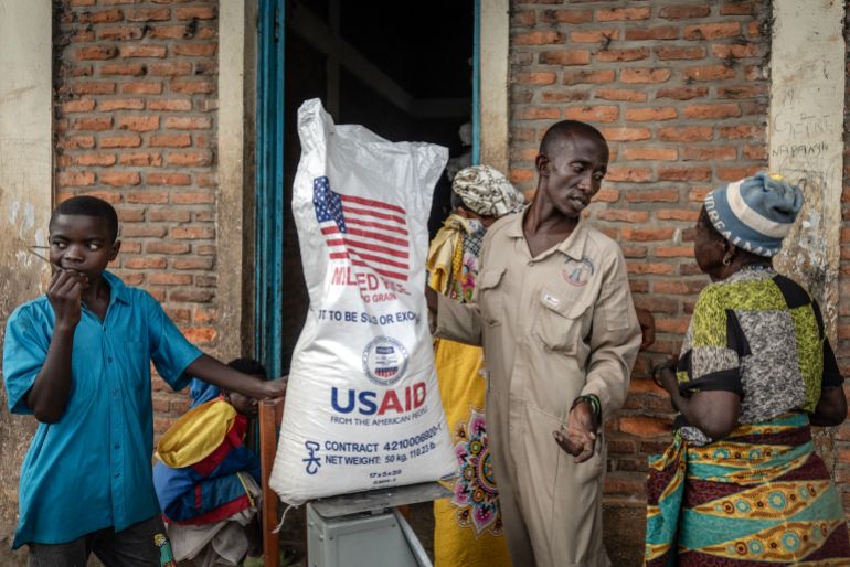 A Burundian official from the Office for the Protection of Refugees speaks with newly arrived Congolese refugees awaiting relocation while weighing a sack of rice delivered by the now-dismantled United States Agency for International Development (USAID) at the Cishemere Transit Centre near Buganda, on May 6, 2025