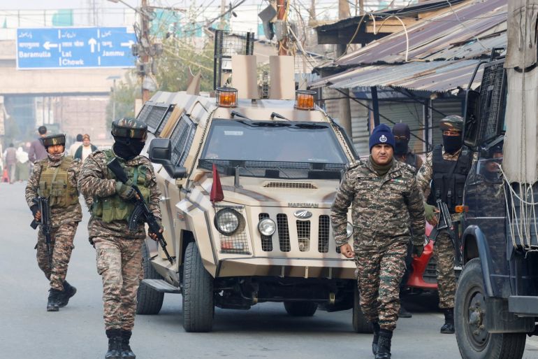 Indian security forces walking in front of a military jeep.