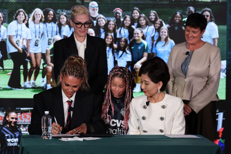 Trinity Rodman (front left) of the Washington Spirit signs a contract extension under the watchful eye of the club’s owner, Michele Kang