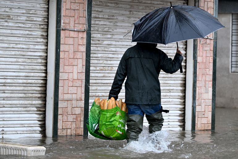 A man carries a bag of bread as he wades through floodwaters , in La Goulette near the capital Tunis, on January 20, 2026.
