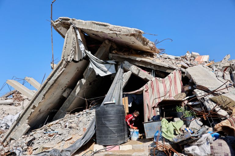A displaced Palestinian girl who live amongst the rubble and debris of homes and businesses destroyed by the Israeli military in over two years of military strikes on the Gaza Strip enclave, fills a container with water from a hose pipe in Jabalia refugee camp, in the northern Gaza Strip on January 17, 2026.