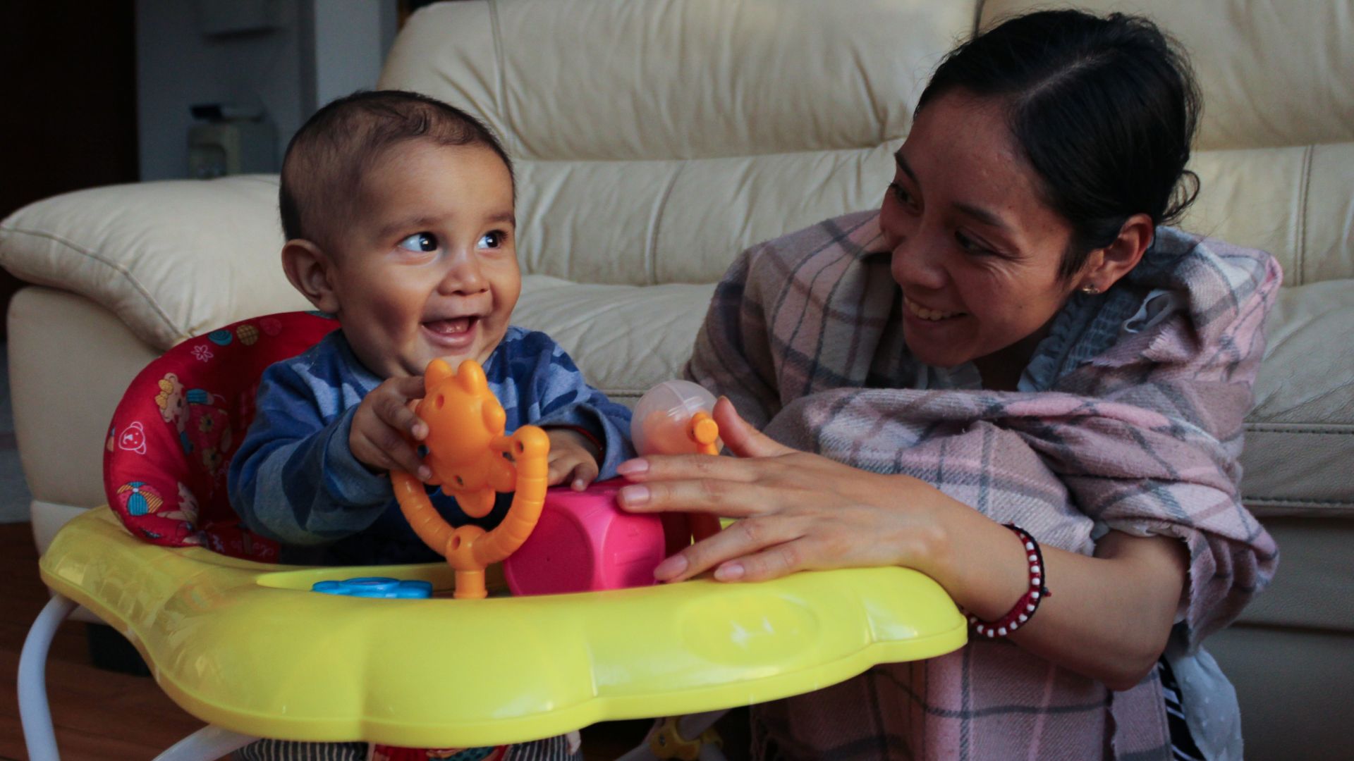 Seated in a play chair, Juan de Jesús laughs as he spins a small twirly toy, while his mother, Luisa, smiles beside him_-1773831295