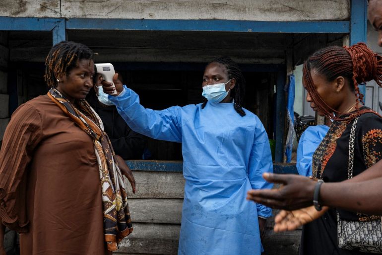 A health worker takes the temperature of a woman passing through the Kanyaruchinya checkpoint, as authorities and aid agencies intensify efforts to contain a new Ebola outbreak involving the Bundibugyo strain, in the northern entry into the city of Goma, North Kivu province, the Democratic Republic of the Congo