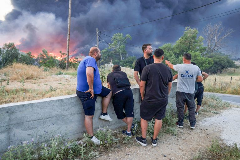 Local residents look at a burning recycling factory, after a wildfire threatened homes and burned businesses in Oreokastro, on the outskirts of Thessaloniki, Greece, July 5, 2026. REUTERS/Alexandros Avramidis