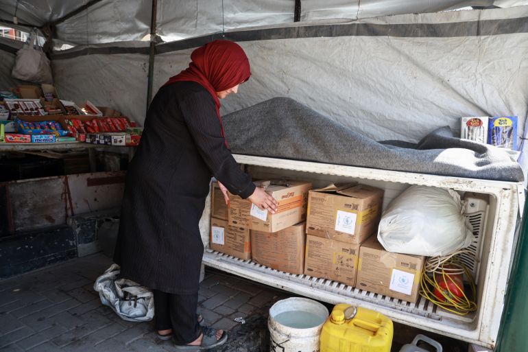 Malak has turned her unused refrigerator into a table with shelves to store aid boxes and household items.[Abdelhakim Abu Riash/ Al Jazeera] 